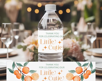 May include: A clear plastic water bottle with a white label featuring orange fruit illustrations on branches, green leaves, and the text "THANK YOU FOR CELEBRATING OUR Little Cutie" in orange and green lettering with small four-pointed star accents.