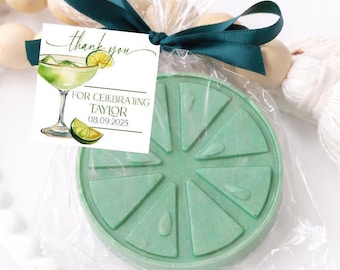 May include: A round, light green lime-shaped soap packaged in a clear plastic bag tied with a dark green ribbon. A square tag attached to the ribbon features a watercolour illustration of a margarita and the text: thank you FOR CELEBRATING TAYLOR 08.09.2025.