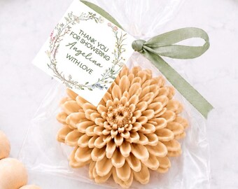 May include: A beige flower-shaped soap inside a clear plastic bag tied with a green ribbon. A square white tag is attached, featuring a floral wreath illustration and the text: THANK YOU FOR SHOWERING Angelina WITH LOVE.