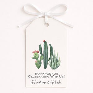 May include: A rectangular white paper gift tag with a white ribbon bow at the top. The tag features a watercolor illustration of three green cacti with small pink flowers. The text reads: THANK YOU FOR CELEBRATING WITH US! Heather & Nick.