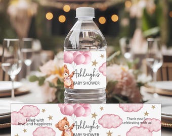 May include: A clear plastic water bottle with a white label featuring a brown teddy bear, pink balloons, and gold stars. The text reads Ashleigh's BABY SHOWER, Filled with love and happiness, and Thank you for celebrating with us.