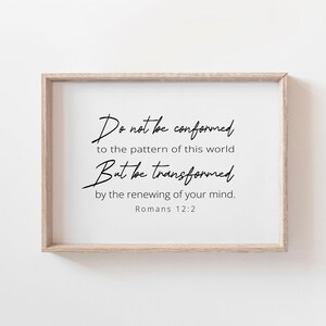 May include: A framed print with the text "Do not be conformed to the pattern of this world But be transformed by the renewing of your mind. Romans 12:2" in black script. The frame is a light brown color.