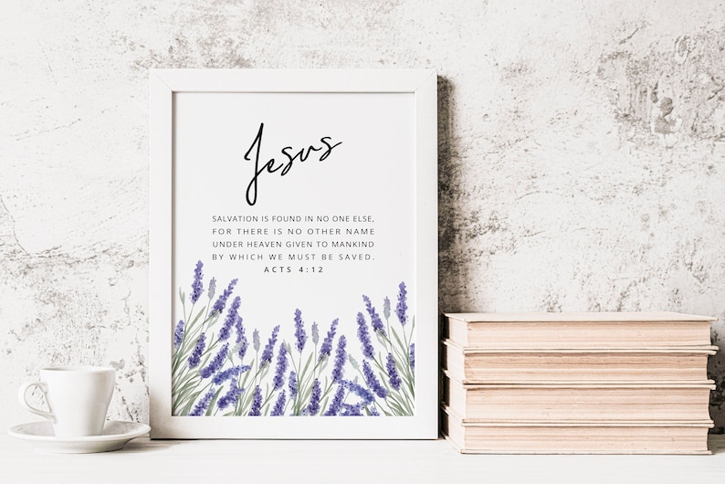 K&ouml;nnte beinhalten: Wei&szlig; gerahmter Druck mit dem Wort "Jesus" in Schrift und einem Bibelvers &uuml;ber die Erl&ouml;sung. Der untere Teil des Drucks zeigt eine Aquarellillustration von lila Lavendel. Ein Stapel B&uuml;cher und eine Teetasse befinden sich daneben.