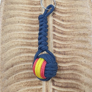 May include: A black and red rope keychain with a knotted ball at the end. The ball is decorated with yellow and red stripes.