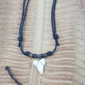 May include: A black cord necklace with a shark tooth pendant. The tooth is white and has a silver wire wrapped around it. The cord has brown wooden beads.