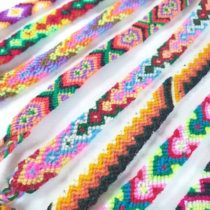 Puede incluir: Una colección de pulseras de amistad coloridas con varios patrones geométricos. Las pulseras están hechas con hilo tejido y presentan una variedad de colores, incluyendo rojo, verde, azul, amarillo y morado.