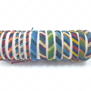 Pode incluir: Uma coleção de pulseiras de amizade coloridas com vários padrões geométricos. As pulseiras são feitas com fios tecidos em tons de azul, vermelho, amarelo, verde e preto.
