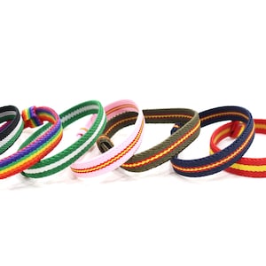 May include: A selection of woven bracelets in a variety of colours. The bracelets display striped patterns in combinations such as black, white, green, rainbow, pink, yellow, and blue. These bracelets are a vibrant and stylish accessory.