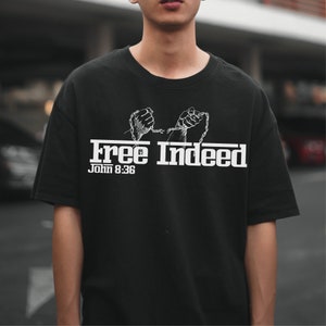 May include: Black t-shirt with a white graphic of two hands breaking free from chains. The text "Free Indeed" and "John 8:36" is printed below the graphic.