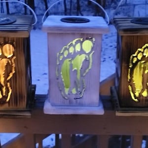 May include: Three wooden lanterns with a footprint design. The lanterns are lit and glow yellow. The lanterns are on a wooden railing.