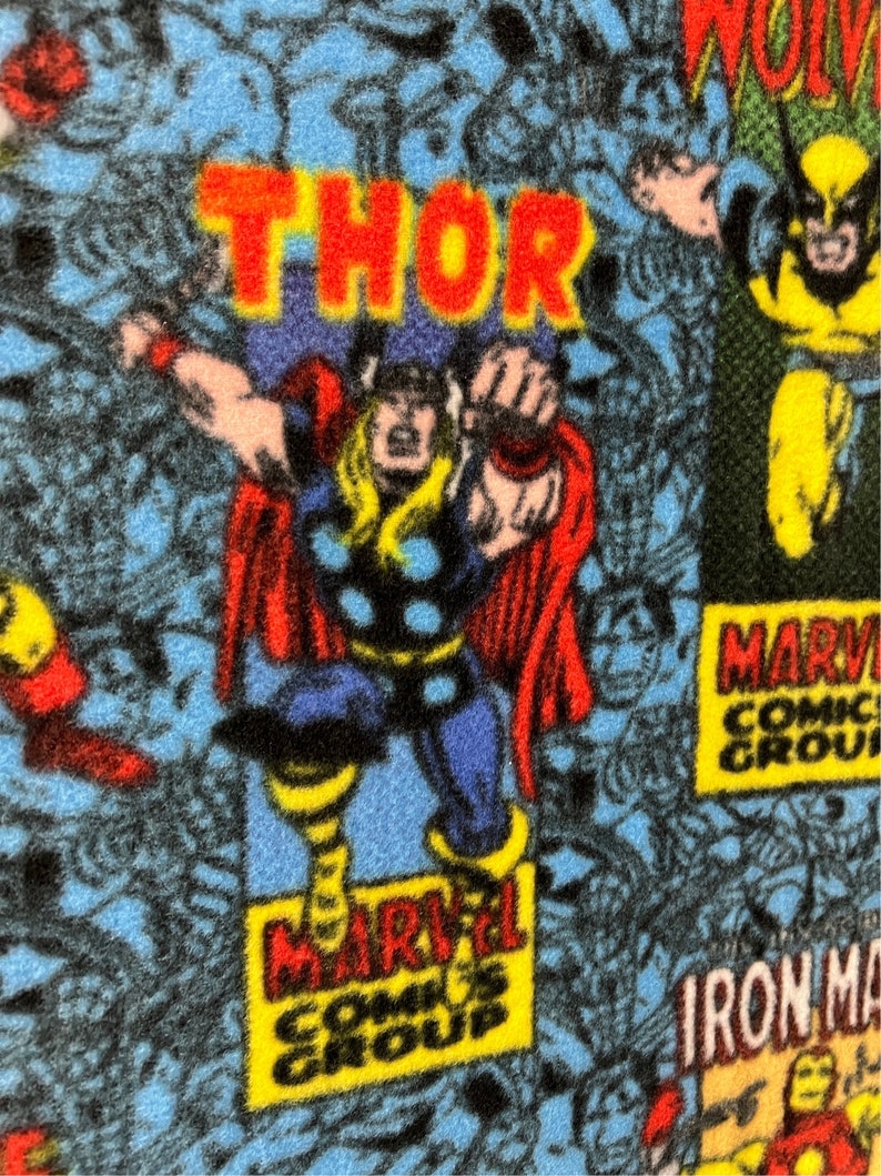 Peut inclure: Un tissu bleu avec un motif de bande dessin&eacute;e mettant en sc&egrave;ne des personnages Marvel comme Thor, Wolverine et Iron Man. Le tissu porte l'inscription "Marvel Comics Group".