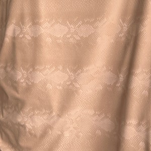 Puede incluir: Primer plano de una tela beige con un sutil estampado de piel de serpiente. La tela tiene una textura suave y sedosa.