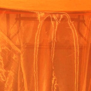 Könnte beinhalten: Orangefarbener, durchsichtiger Tischläufer, der über einen Tisch gelegt ist. Der Tischläufer ist durchscheinend und hat einen leichten Schimmer.