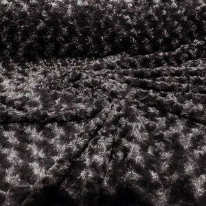 Puede incluir: Tela de rosetas gris oscuro con una superficie texturizada y afelpada. La tela presenta un patrón repetitivo de pequeñas rosetas en relieve, creando un aspecto suave y dimensional. Adecuada para diversos proyectos de manualidades y costura.