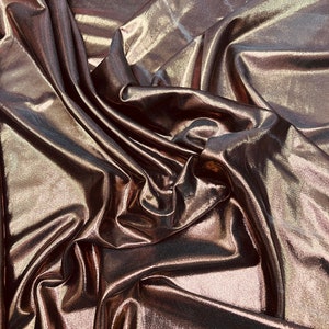 May include: Close-up of a metallic bronze fabric with a shimmery finish. The fabric is draped and folded, showcasing its texture and sheen.
