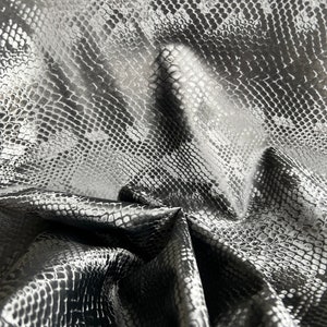 May include: Black faux leather fabric with a snakeskin pattern. The fabric is wrinkled and folded.