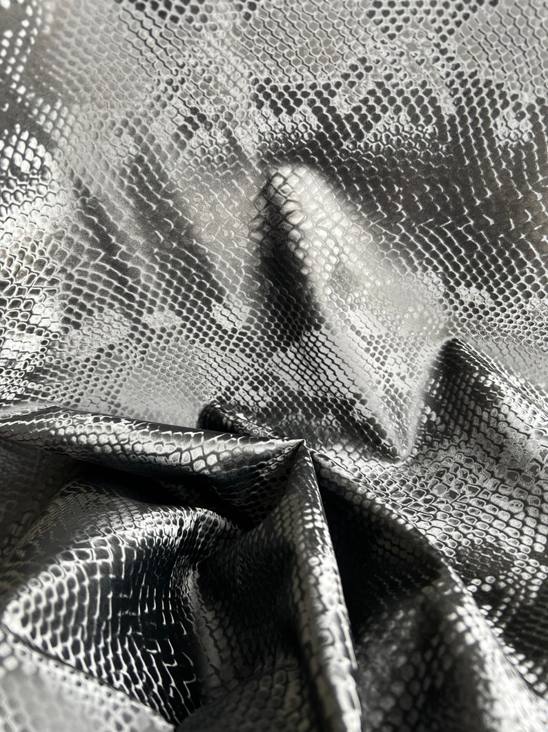 May include: Black faux leather fabric with a snakeskin pattern. The fabric is wrinkled and folded.