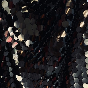 May include: Black fabric with a pattern of overlapping round sequins. The sequins have a metallic sheen and are arranged in a diagonal pattern.