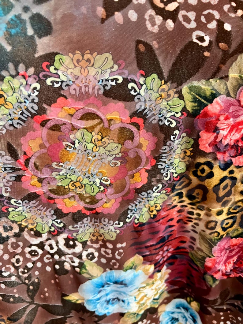 May include: A brown sheer fabric with a colorful floral pattern. The fabric features a variety of flowers, including roses, daisies, and other floral designs. The fabric also has a leopard print pattern.
