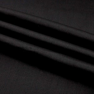 May include: Black fabric with a smooth, silky texture. The fabric is folded in a way that creates soft, flowing lines.
