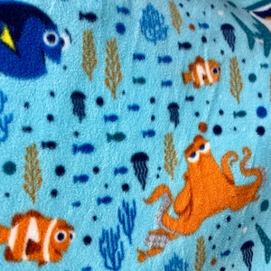 May include: A blue and orange fleece blanket with a repeating pattern of fish, seaweed, and jellyfish. The fish include Dory, Nemo, and a shark.