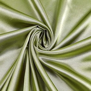 May include: Close-up of a swatch of olive green satin fabric. The fabric is folded and draped, creating a swirling pattern. The satin has a smooth, shiny surface, reflecting light and highlighting the folds and textures.
