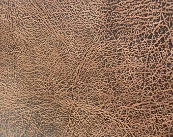 Op de afbeelding: Close-up van een getextureerd oppervlak met een distressed leer-uitstraling. De kleur is een mix van bruin en zwart, met een netwerk van fijne, lichtbruine lijnen die een gedetailleerd patroon creëren.