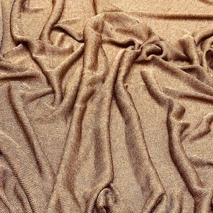 May include: Close-up of a brown, textured fabric with a subtle shimmer. The fabric is draped and folded, creating a soft and luxurious look.