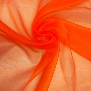 May include: Vibrant orange sheer fabric, elegantly draped and swirled. The translucent material creates a play of light and shadow, with bright orange hues dominating the composition. The fabric's texture is smooth and flowing, suggesting a lightweight quality.