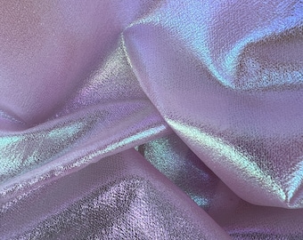 Puede incluir: Primer plano de una tela iridiscente de color morado claro con una superficie texturizada. La tela está doblada y drapeada, creando pliegues y curvas suaves.