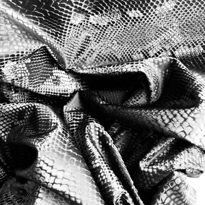 May include: Black and white textured fabric with a snake skin pattern. The fabric is wrinkled and folded.