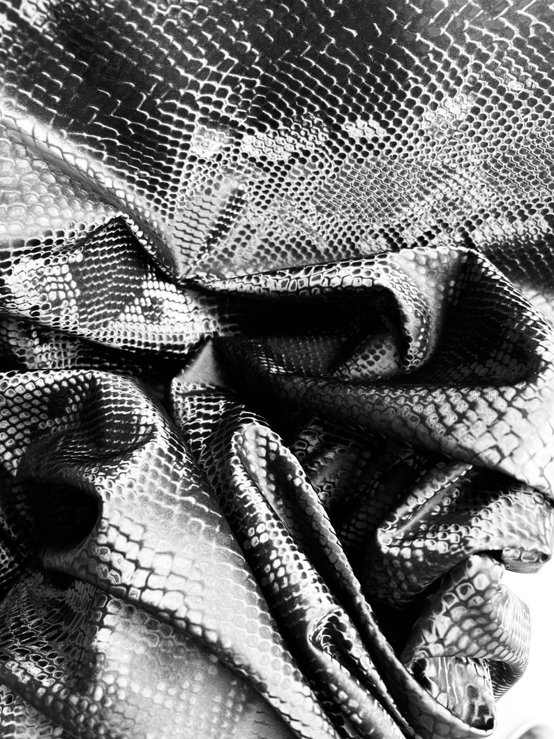 May include: Black and white textured fabric with a snake skin pattern. The fabric is wrinkled and folded.