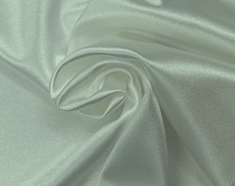 Könnte beinhalten: Nahaufnahme eines glatten, weißen Stoffes mit einem dezenten Glanz. Der Stoff ist drapiert und gefaltet und zeigt seine weiche Textur.