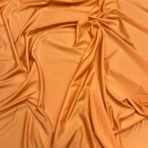 May include: A solid orange fabric with a smooth, slightly reflective surface. The material is draped in soft, flowing folds, creating deep shadows and highlights across the texture, emphasizing the consistent color and flexible nature of the textile.