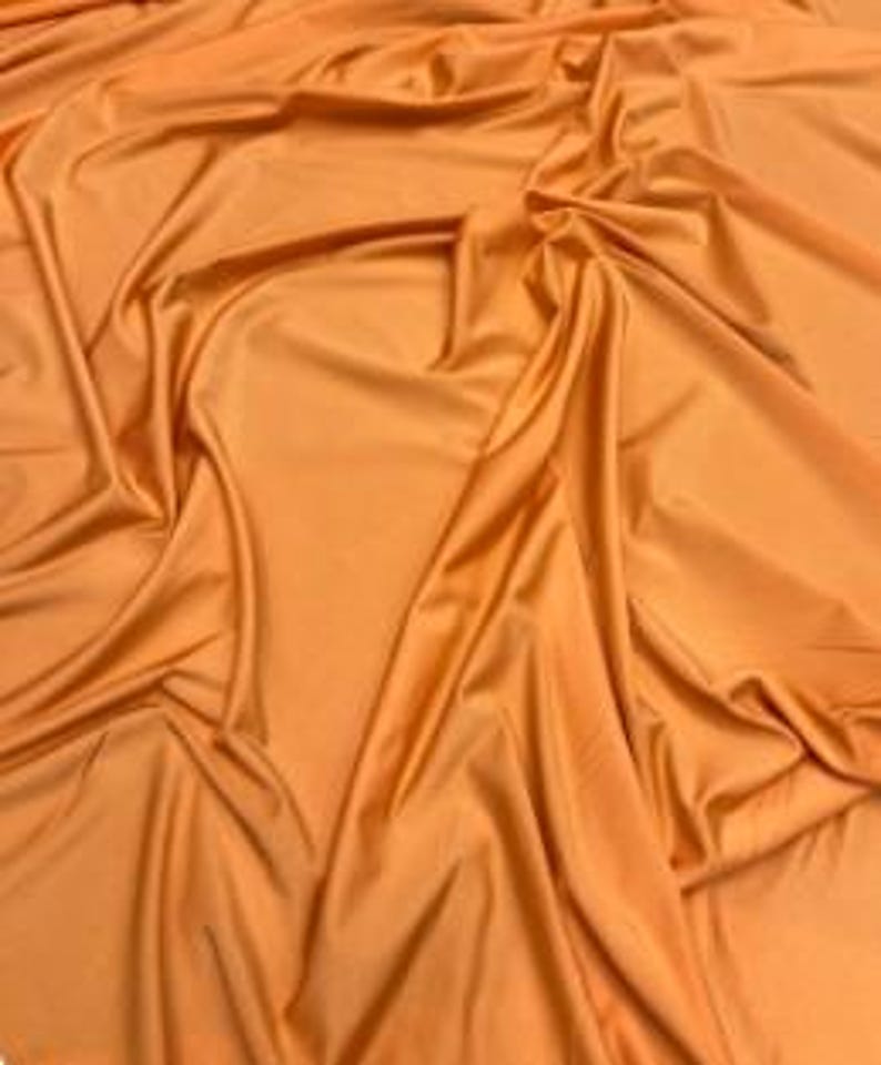 K&ouml;nnte beinhalten: Ein einfarbiger orangefarbener Stoff mit einer glatten, leicht reflektierenden Oberfl&auml;che. Das Material ist in weichen, flie&szlig;enden Falten drapiert, die tiefe Schatten und Glanzlichter auf der Textur erzeugen und die Farbe und Flexibilit&auml;t betonen.
