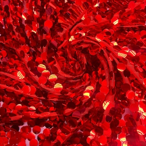 Può includere: Primo piano di tessuto di paillettes rosse. Il tessuto è densamente ricoperto di paillettes rotonde e lucenti, creando una superficie strutturata. Le paillettes riflettono la luce, conferendo al tessuto un aspetto scintillante. Il tessuto è probabilmente utilizzato per abbigliamento o scopi decorativi.