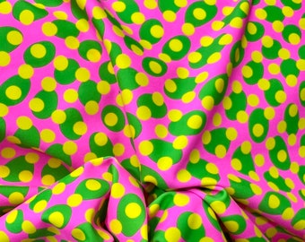May include: Pink fabric with a repeating pattern of green and yellow circles. The fabric is folded and draped, showing the pattern from different angles.