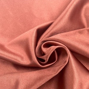 May include: Close-up of a smooth, rust-colored fabric with a subtle sheen. The fabric is folded and draped, showcasing its soft texture.