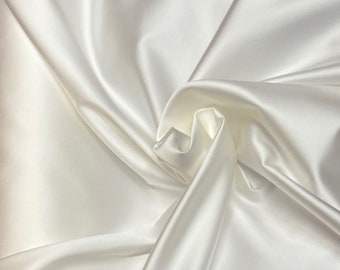 Könnte beinhalten: Nahaufnahme eines weißen Satinstoffs mit sanften Falten und glänzendem Glanz. Der Stoff ist drapiert, wodurch Schatten und Glanzlichter entstehen, die seine glatte Textur hervorheben. Der Gesamteindruck ist von Eleganz und Luxus geprägt.