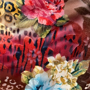 May include: A close-up of a fabric with a floral and animal print. The fabric features a large pink rose, a smaller blue rose, and a leopard print pattern. The fabric is a mix of red, blue, pink, yellow, and brown.