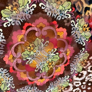 May include: Close-up of a brown fabric with a colorful floral pattern. The fabric has a shiny, almost iridescent, quality. The pattern includes flowers, leaves, and swirls.