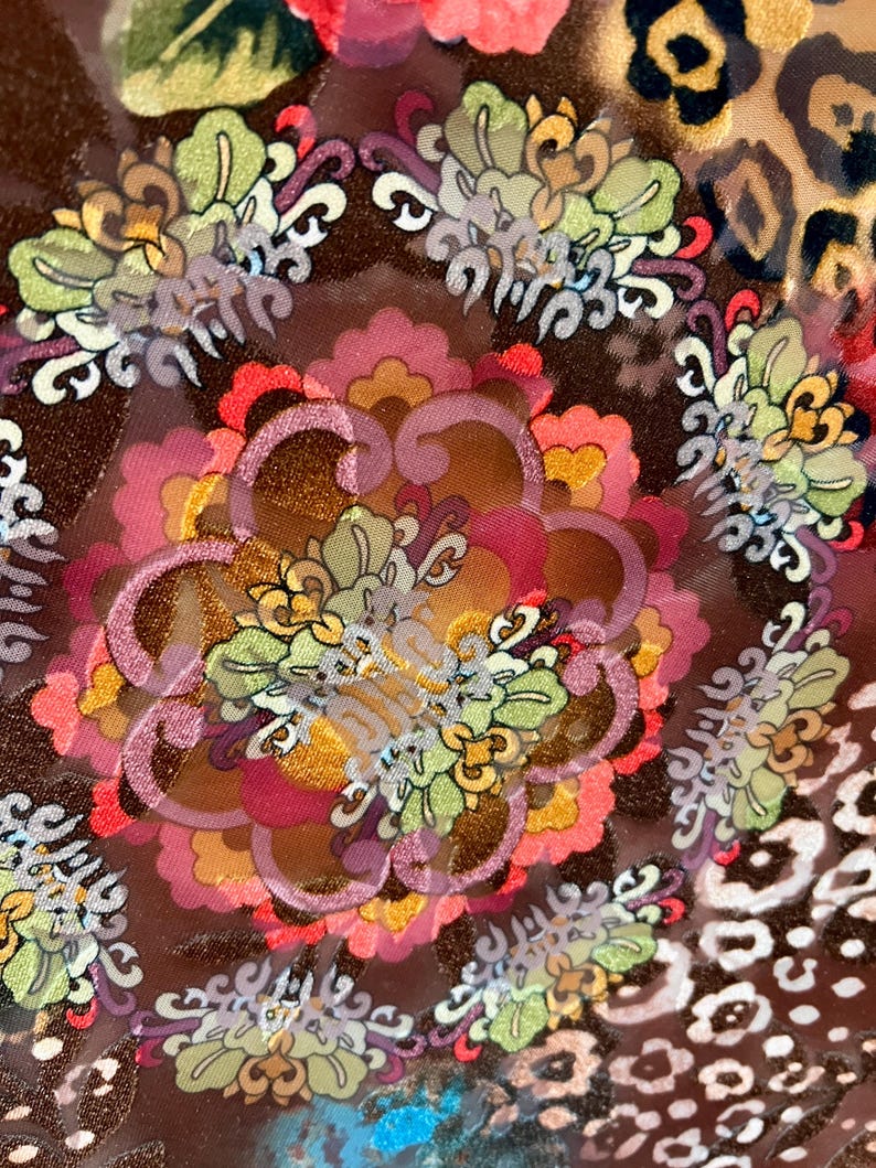 May include: Close-up of a brown fabric with a colorful floral pattern. The fabric has a shiny, almost iridescent, quality. The pattern includes flowers, leaves, and swirls.