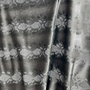 May include: Close-up of a black and silver fabric with a snakeskin pattern. The fabric is textured and has a slight sheen.