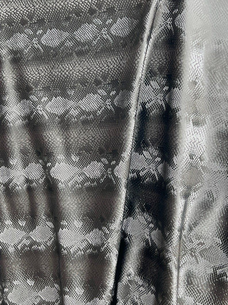 May include: Close-up of a black and silver fabric with a snakeskin pattern. The fabric is textured and has a slight sheen.