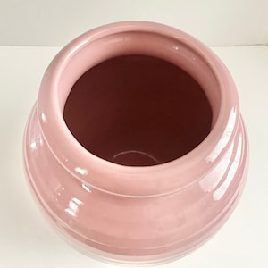 May include: A pink ceramic vase with a rounded shape and a smooth, glossy finish. The vase has a wide opening and a slightly flared rim.