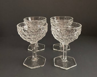 Pode incluir: Quatro taças de champanhe de vidro transparente com um padrão texturizado em forma de diamante. As taças têm uma taça larga e uma haste longa e fina.