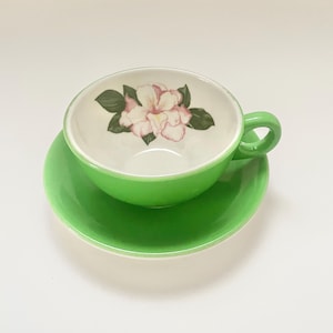 May include: A white ceramic mug with a black handle and the text "But First, Coffee" in a bold, black font. The mug is set against a blurred background, suggesting a cozy setting.