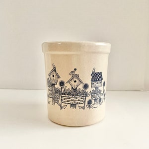 Puede incluir: Un porta utensilios de cerámica de color crema con un diseño en blanco y negro de casas para pájaros, girasoles y pájaros. El diseño recuerda a un pintoresco jardín de campo.
