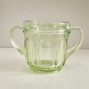 以下が含まれることがあります： 2つの取っ手のある透明な緑色のガラス製の砂糖入れ。ボウルはフルーテッドデザインで、丸い底になっています。