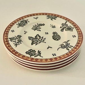 以下が含まれることがあります： 花とパイナップルのデザインが施された、白いセラミックプレート4枚のスタック。 プレートには茶色とタン色のチェック柄のボーダーと、黒とグレーの花と果物のモチーフがあります。 各プレートの直径は約20cmです。